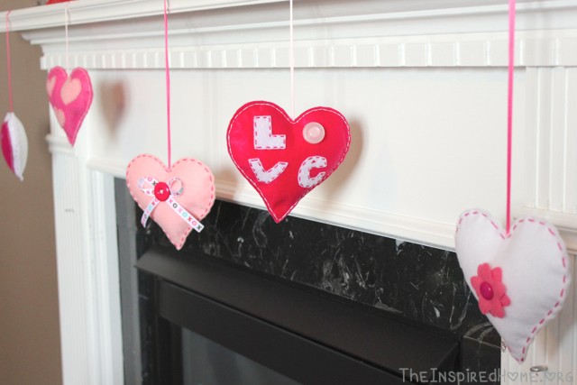 Valentine's Day Felt Hearts hung from the fireplace mantel. Tutorial available at TheInspiredHome.org